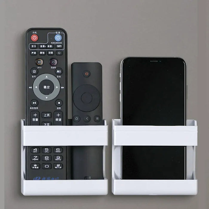 Suporte de parede branco minimalista instalado em uma parede cinza, segurando um celular e um controle remoto.